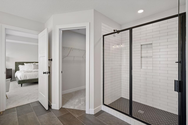 ensuite bathroom featuring a textured ceiling, connected bathroom, baseboards, a spacious closet, and a stall shower