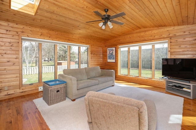 living room featuring lofted ceiling with skylight, wood walls, light hardwood / wood-style flooring, wooden ceiling, and ceiling fan