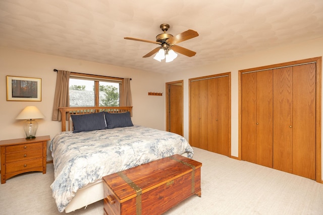 bedroom featuring ceiling fan, light colored carpet, and two closets