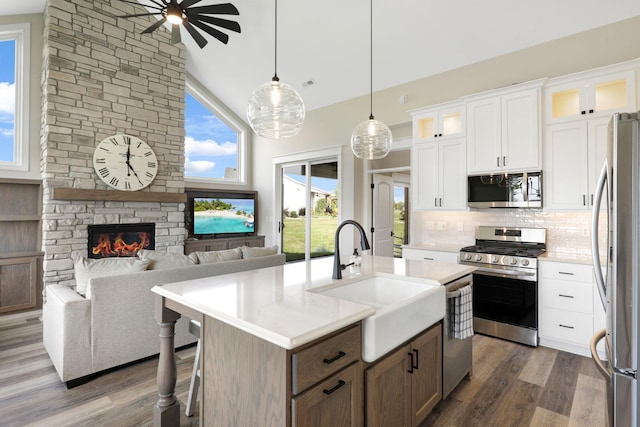 kitchen featuring a center island with sink, stainless steel appliances, dark wood-type flooring, and a fireplace