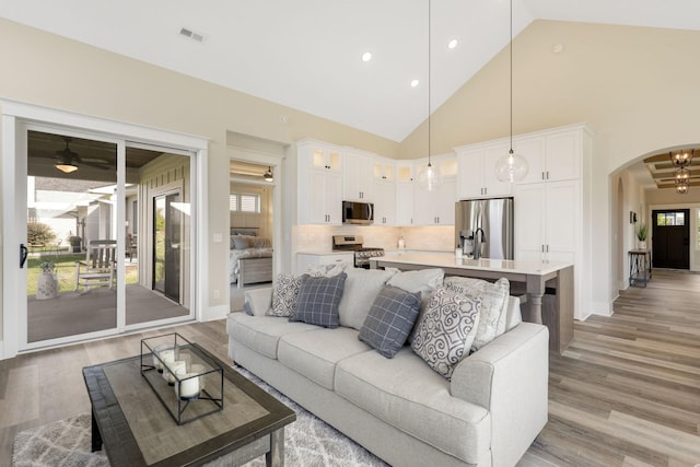 living room with ceiling fan, high vaulted ceiling, light hardwood / wood-style floors, and plenty of natural light