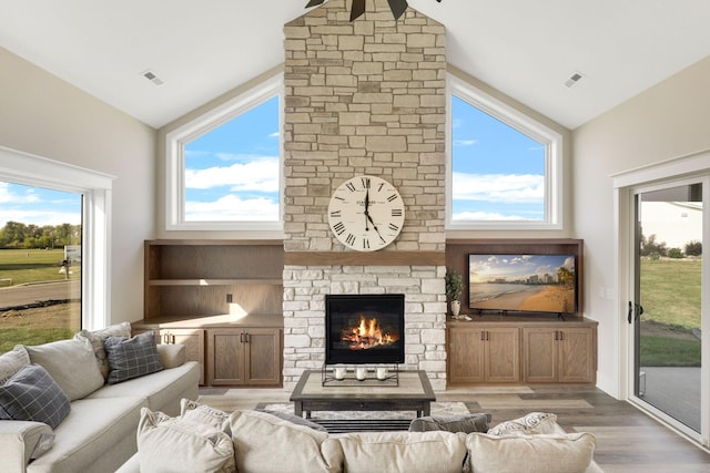 living room featuring a stone fireplace, high vaulted ceiling, and light wood-type flooring