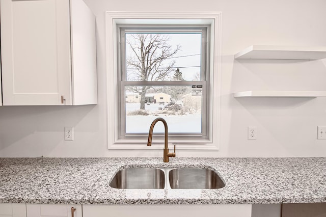 kitchen with sink, light stone counters, and white cabinetry