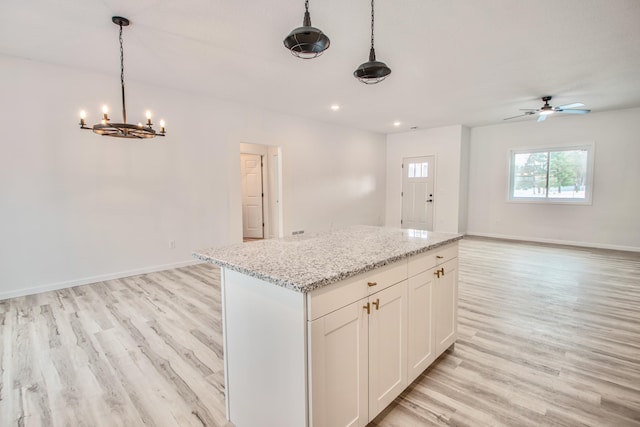 kitchen featuring decorative light fixtures, light stone counters, white cabinetry, and a center island