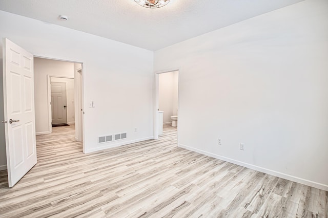 unfurnished bedroom with light wood-type flooring, ensuite bathroom, and a textured ceiling