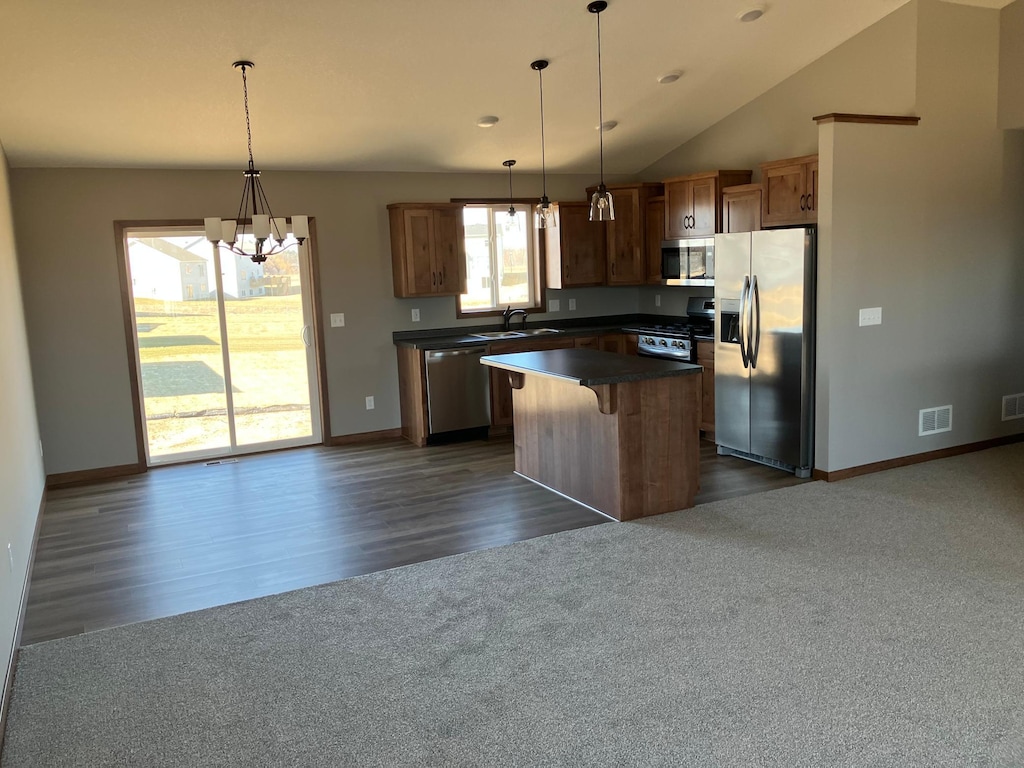 kitchen with hanging light fixtures, appliances with stainless steel finishes, a breakfast bar, vaulted ceiling, and a kitchen island