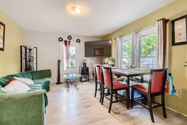 dining room featuring plenty of natural light, a textured ceiling, a wood stove, and light wood-type flooring