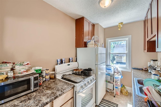 kitchen with light tile flooring, dark stone countertops, white appliances, and a textured ceiling