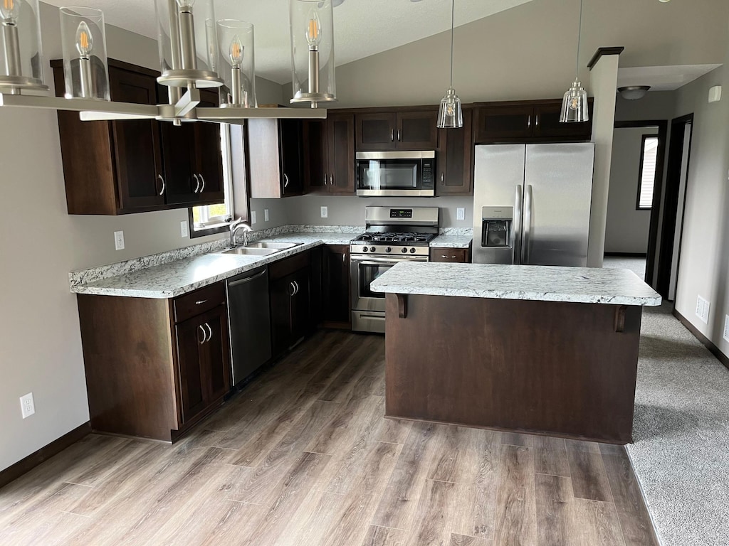 kitchen featuring appliances with stainless steel finishes, pendant lighting, a kitchen island, lofted ceiling, and light carpet