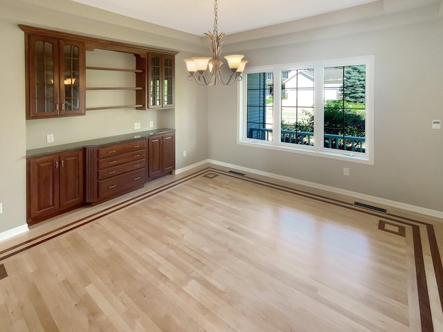 unfurnished dining area featuring light wood-type flooring, a raised ceiling, and a notable chandelier