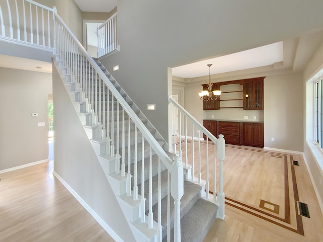 stairway with a towering ceiling, wood-type flooring, and an inviting chandelier