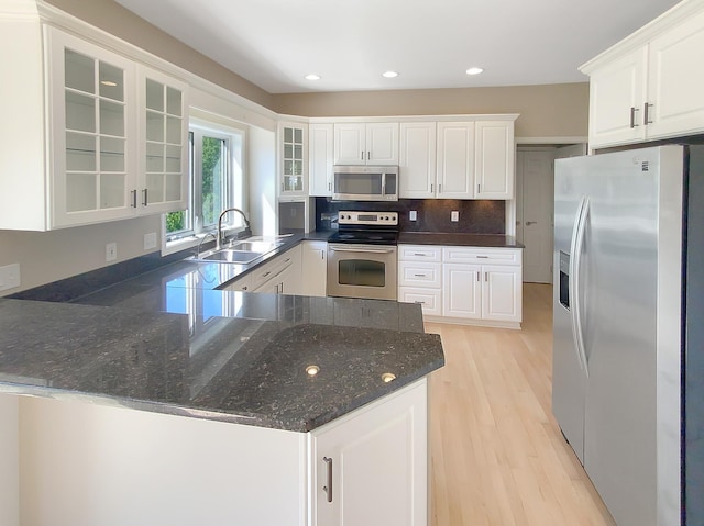 kitchen with light wood-type flooring, tasteful backsplash, stainless steel appliances, sink, and white cabinets