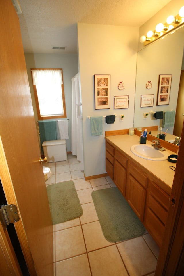 bathroom with a textured ceiling, toilet, vanity with extensive cabinet space, and tile flooring