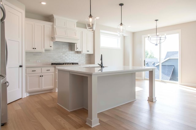 kitchen featuring an island with sink, white cabinets, and decorative light fixtures