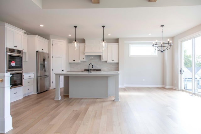 kitchen with pendant lighting, white cabinets, sink, stainless steel appliances, and light wood-type flooring