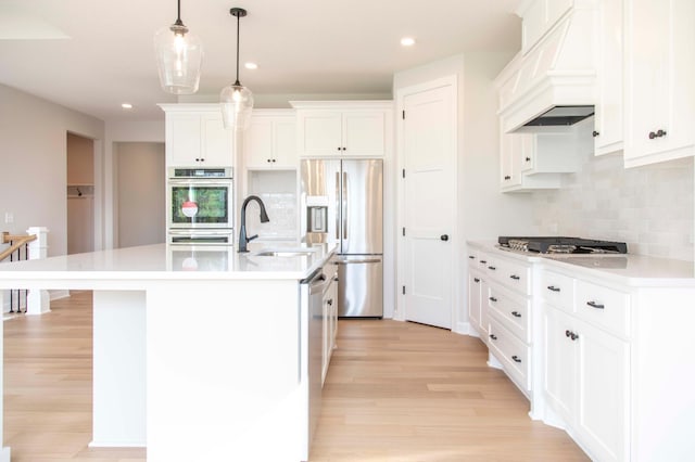 kitchen with sink, stainless steel appliances, an island with sink, white cabinets, and premium range hood