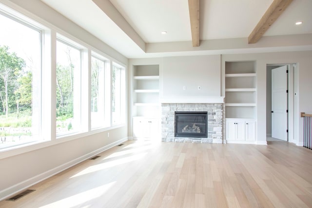 unfurnished living room with built in shelves, light hardwood / wood-style flooring, and a stone fireplace