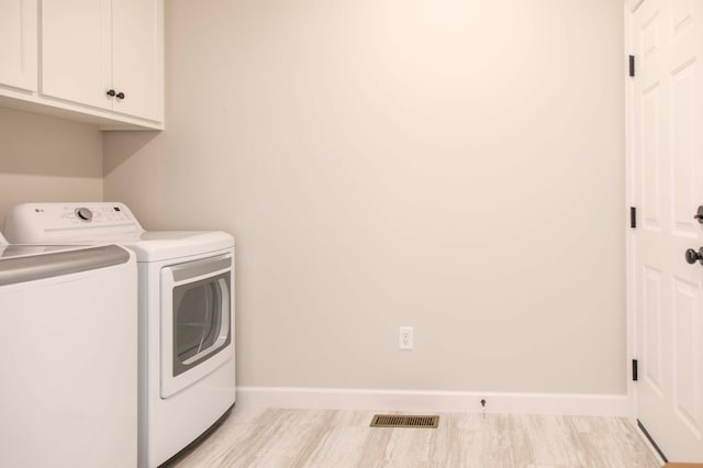 clothes washing area featuring light wood-type flooring, independent washer and dryer, and cabinets