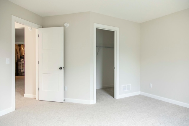 unfurnished bedroom featuring a spacious closet, a closet, and light colored carpet