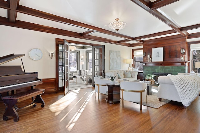 living room with hardwood / wood-style floors, an inviting chandelier, beam ceiling, a tiled fireplace, and coffered ceiling