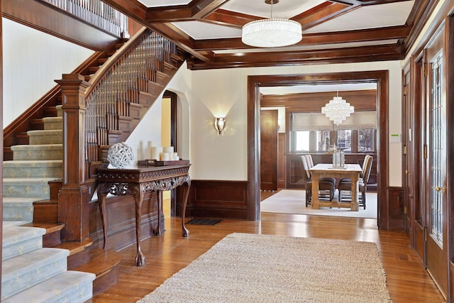 entrance foyer featuring crown molding, an inviting chandelier, coffered ceiling, and hardwood / wood-style flooring