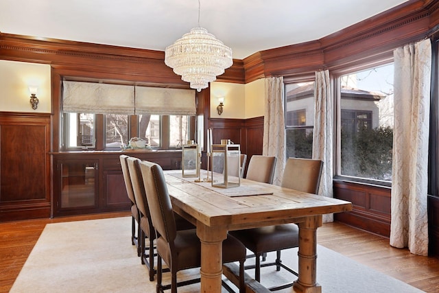 dining room featuring light wood-type flooring, wooden walls, and a notable chandelier