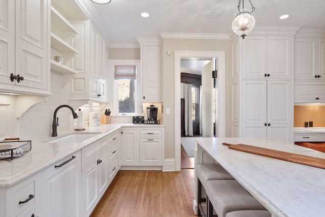 kitchen with light hardwood / wood-style floors, ornamental molding, pendant lighting, white cabinets, and sink