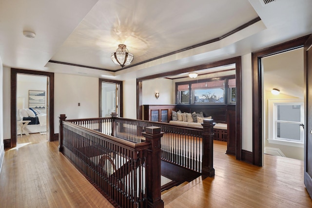 interior space with a crib, light wood-type flooring, a tray ceiling, and ornamental molding