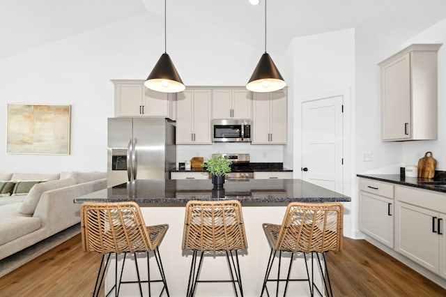 kitchen featuring dark wood-type flooring, decorative light fixtures, a kitchen breakfast bar, a kitchen island, and stainless steel appliances