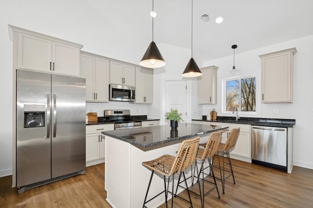 kitchen featuring a breakfast bar area, decorative light fixtures, a center island, light hardwood / wood-style flooring, and appliances with stainless steel finishes