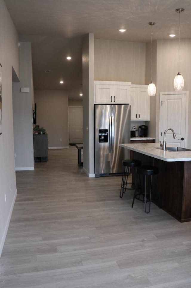 kitchen featuring stainless steel fridge with ice dispenser, light hardwood / wood-style floors, sink, white cabinets, and pendant lighting