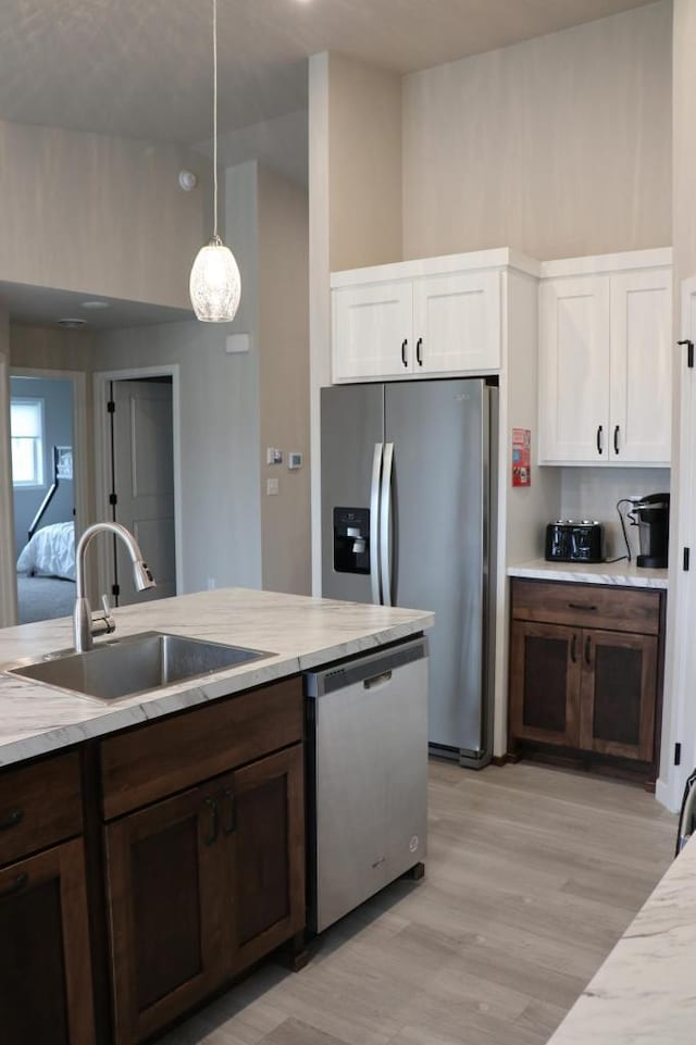 kitchen with light wood-type flooring, white cabinets, appliances with stainless steel finishes, decorative light fixtures, and dark brown cabinetry