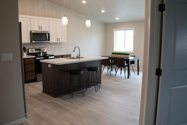 kitchen with appliances with stainless steel finishes, light wood-type flooring, a center island with sink, white cabinets, and pendant lighting