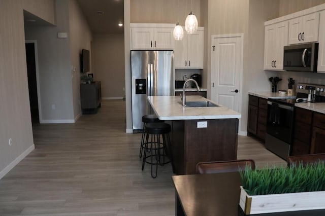 kitchen featuring sink, hanging light fixtures, light hardwood / wood-style floors, stainless steel appliances, and white cabinetry