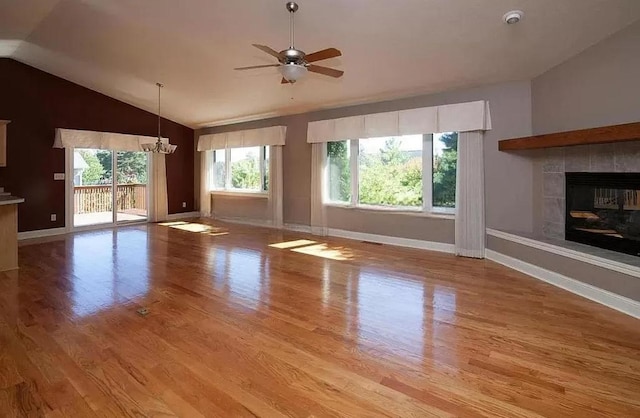 unfurnished living room featuring lofted ceiling, a tiled fireplace, light wood-type flooring, and ceiling fan with notable chandelier