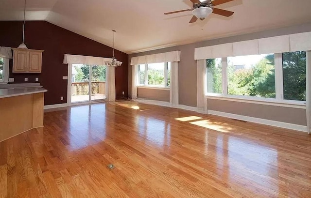 unfurnished living room with ceiling fan with notable chandelier, vaulted ceiling, and light hardwood / wood-style flooring