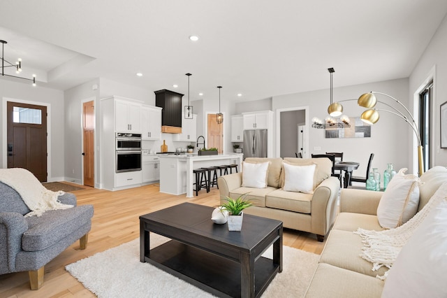 living room featuring light wood-type flooring, a notable chandelier, and sink