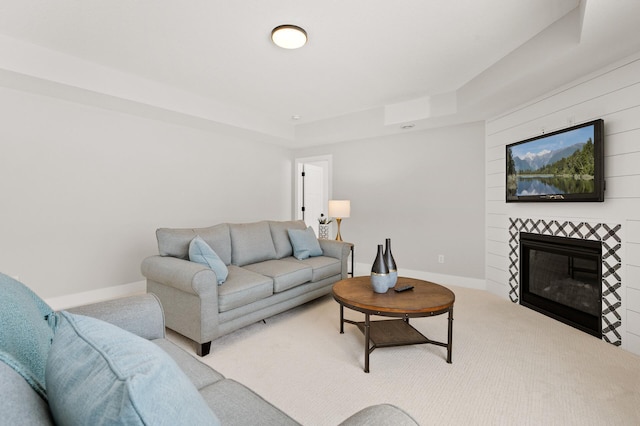 living room with carpet flooring, a raised ceiling, and a tiled fireplace