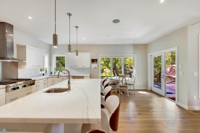 kitchen featuring pendant lighting, stainless steel gas stovetop, white cabinets, sink, and wall chimney exhaust hood