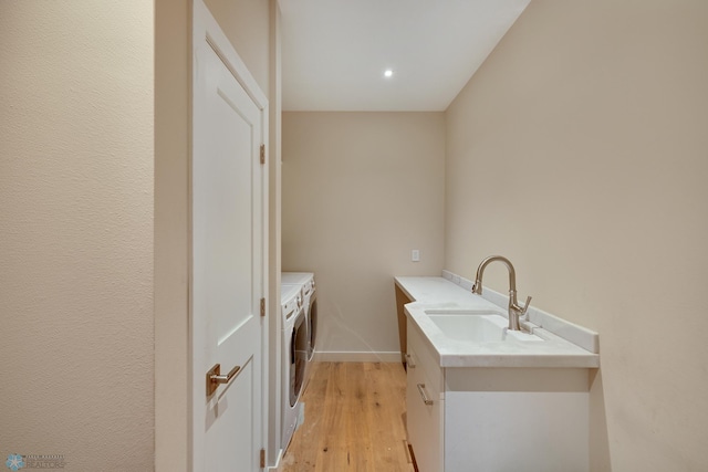 laundry area with light hardwood / wood-style flooring, washer and clothes dryer, and sink