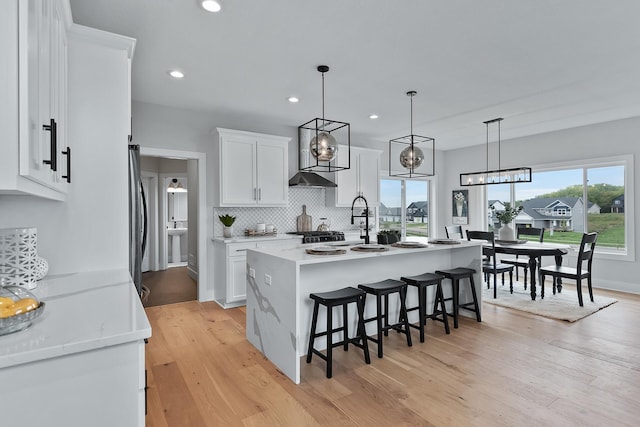 kitchen with light stone counters, a kitchen island with sink, pendant lighting, white cabinets, and light hardwood / wood-style floors