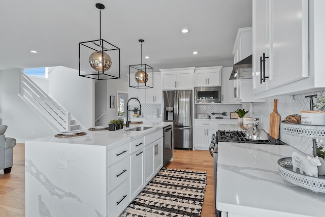 kitchen featuring white cabinets, exhaust hood, an island with sink, and appliances with stainless steel finishes