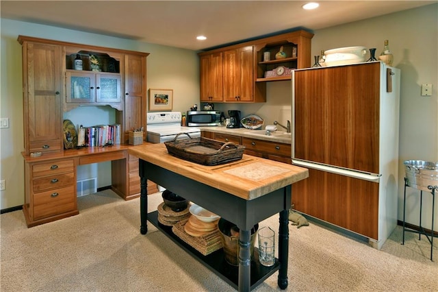 kitchen with sink, light colored carpet, built in desk, and stove