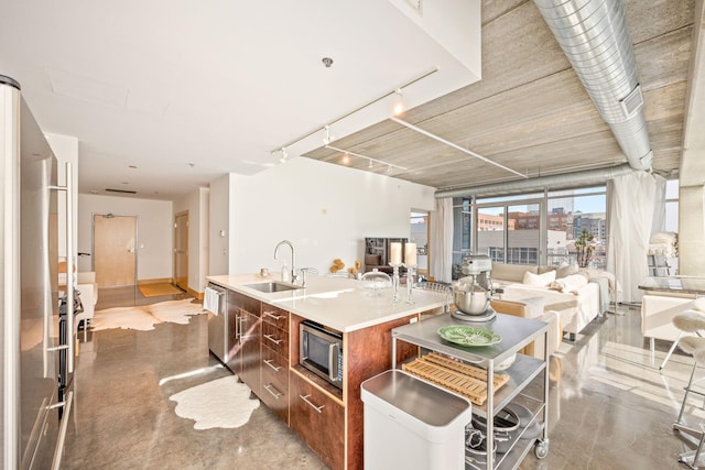 kitchen featuring an island with sink, stainless steel microwave, sink, and concrete floors