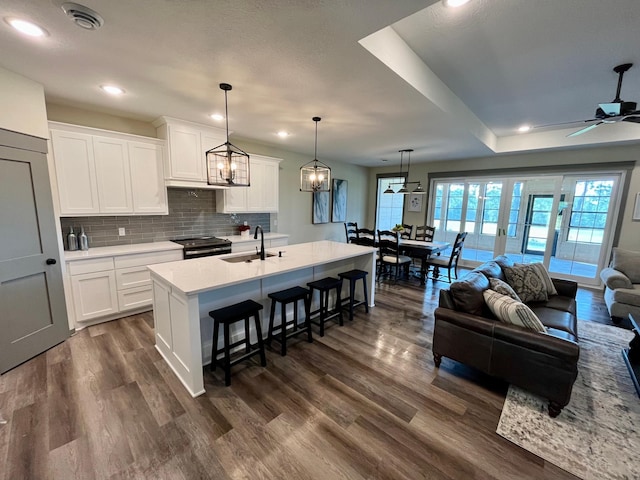 kitchen featuring white cabinetry, a center island with sink, ceiling fan, hanging light fixtures, and sink