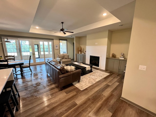 living room featuring ceiling fan, a tray ceiling, and dark hardwood / wood-style flooring