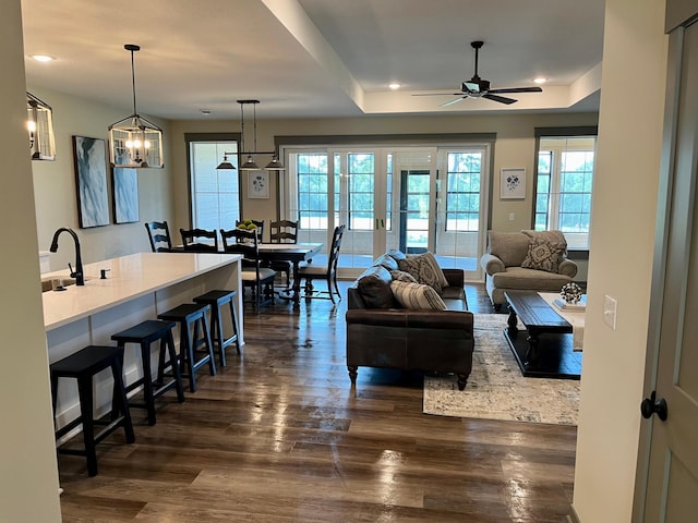 living room featuring ceiling fan with notable chandelier, sink, a tray ceiling, and dark hardwood / wood-style flooring