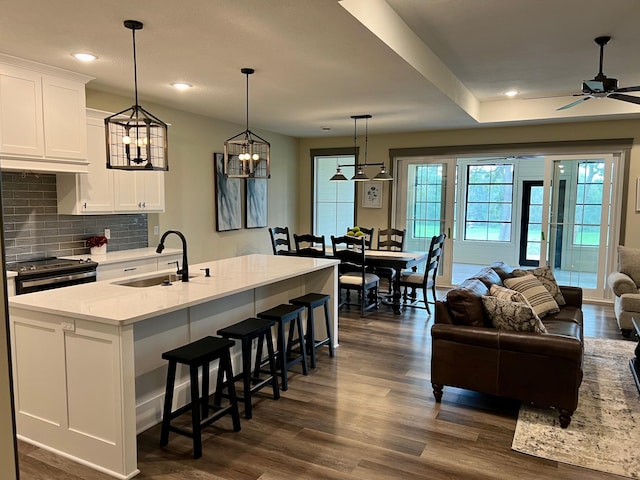 kitchen with white cabinetry, an island with sink, hanging light fixtures, ceiling fan with notable chandelier, and sink