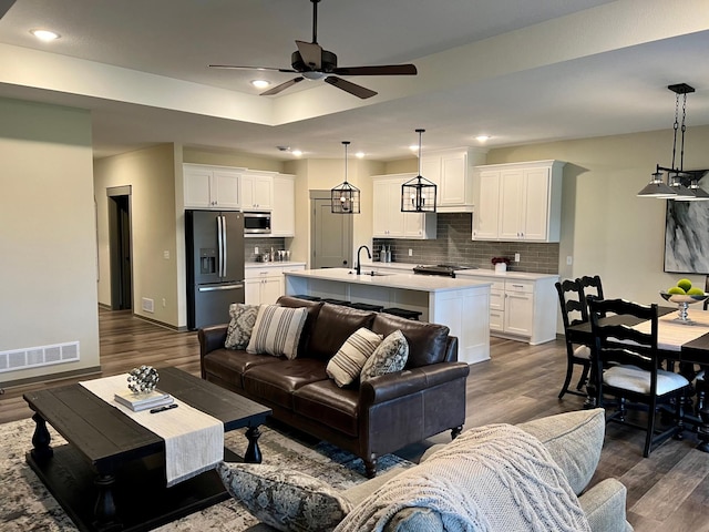 living room with ceiling fan with notable chandelier, sink, dark hardwood / wood-style floors, and a tray ceiling