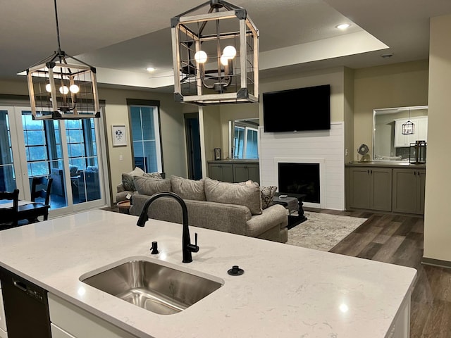 kitchen with pendant lighting, a raised ceiling, a large fireplace, sink, and an inviting chandelier